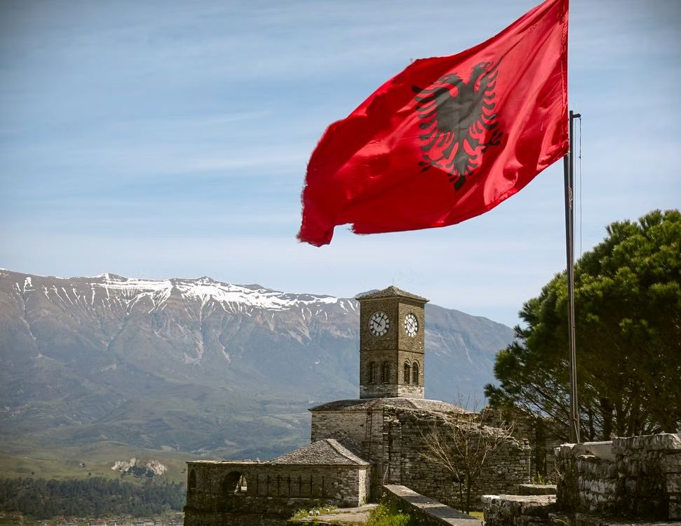 Drapeau albanais flottant devant la tour de l'horloge de la citadelle de Gjirokastër, sommets enneigés en arrière-plan