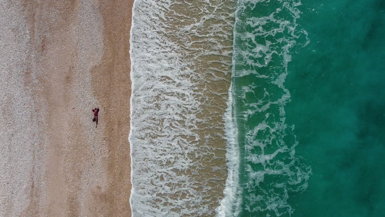 Plage albanaise vue du ciel, bande de sable, écume des vagues et eau turquoise, une personne allongée sur le sable