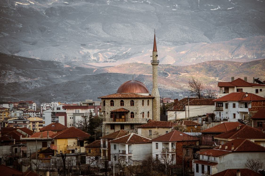 Village albanais aux toits de tuiles rouges et mosquée, au pied de montagnes