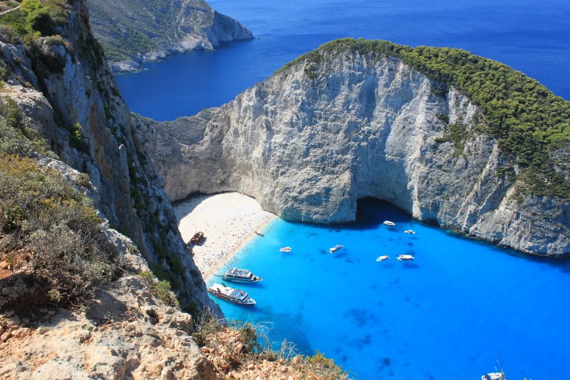 Plage du Naufrage (Navagio) à Zakynthos, crique de sable blanc et eau turquoise au pied de hautes falaises blanches, vue du ciel